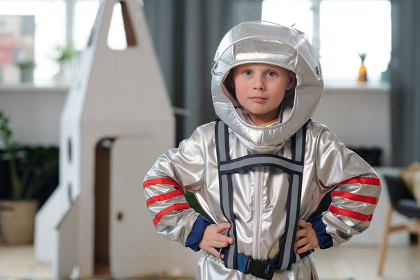 Портрет маленького мальчика в костюме космонавта, смотрящего в камеру во время игры дома - Фото, изображение