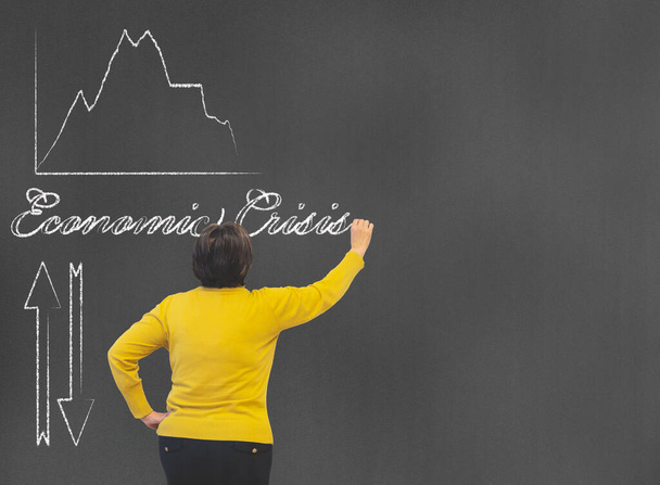 Kobieta w średnim wieku pisząca na tablicy z kredą pojęcia kryzysu gospodarczego ze strzałkami i diagramem finansowym z koncepcją przestrzeni kopiującej economia - Zdjęcie, obraz
