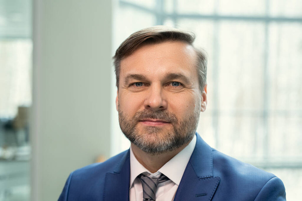 Portrait of smiling handsome middle-aged businessman with stubble standing in contemporary office - Fotografie, Obrázek