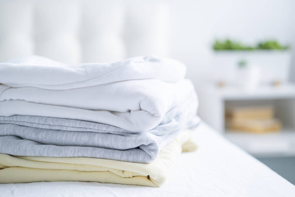 pilha de mulheres camisolas coloridas, capuzes em cores pastel na cama branca. Compras sazonais, lavanderia, conceito de férias - Foto, Imagem