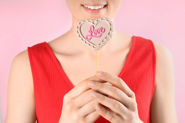 Woman holding heart shaped lollipop made of chocolate on pink background, closeup - Photo, Image