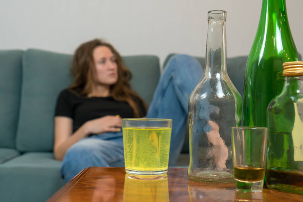 Young dark-haired woman with a hangover will drink a fizzy pill from her head after a wild party at home, trying to prepare for the day ahead. Concept of Monday morning, morning after drinking alcohol - Photo, Image