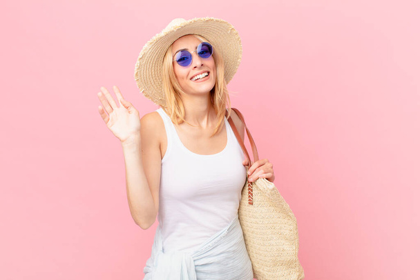 young blonde woman smiling happily, waving hand, welcoming and greeting you. summer concept - Фото, зображення
