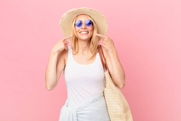 young blonde woman smiling confidently pointing to own broad smile. summer concept - Foto, Bild