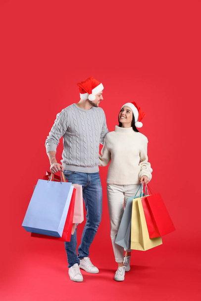 Happy couple with paper bags on red background. Christmas shopping - Foto, Imagem