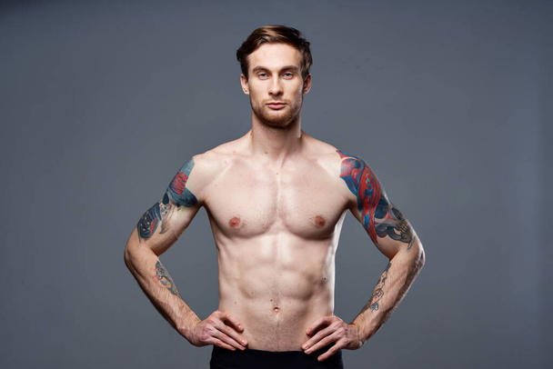 handsome man with a naked pumped-up torso tattoos on his arms holds his hands on his belt - Foto, Bild
