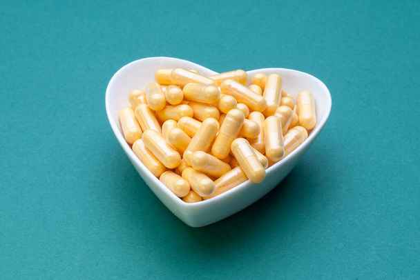 Coenzyme Q10 capsules are arranged in the shape of a heart on a green background - Foto, immagini