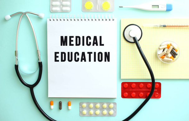 薬や聴診器、黄色いノートの間には、医学教育の文字が入ったノートがきれいに折り畳まれています。医学的概念 - 写真・画像