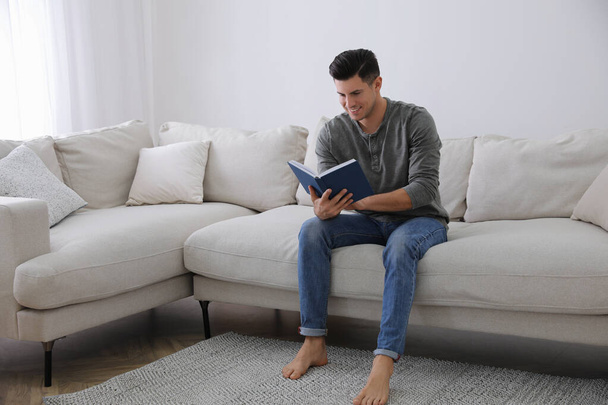 Mann mit Buch sitzt auf bequemem Sofa im Wohnzimmer - Foto, Bild