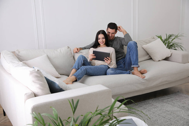 Couple with tablet resting on sofa in living room - Фото, изображение