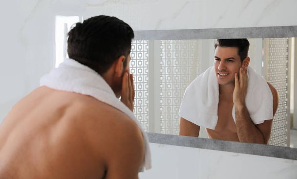 Handsome man touching his smooth face after shaving near mirror in bathroom - Foto, immagini