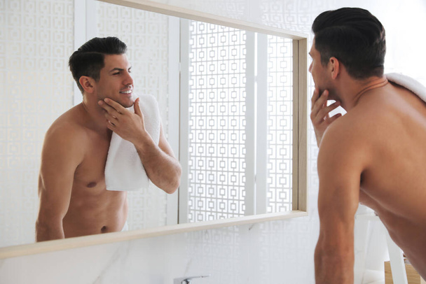 Красивий чоловік торкається свого гладкого обличчя після гоління біля дзеркала у ванній
 - Фото, зображення