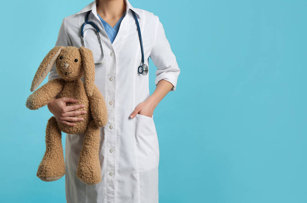 Pediatrician with toy bunny and stethoscope on turquoise background, closeup. Space for text - Fotografie, Obrázek