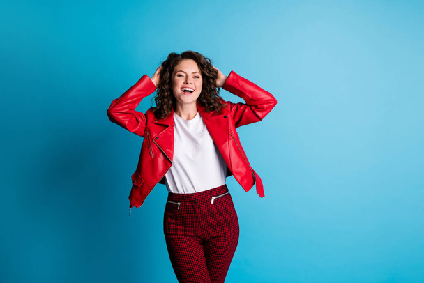 Photo of nice optimistic girl hands in hair wear red jacket pants isolated on blue color background - Φωτογραφία, εικόνα