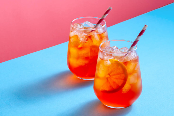 Коктейль Aperol Spritz в стаканах со льдом и апельсиновым ломтиком на модном красочном фоне. Креативное минимальное понятие. - Фото, изображение