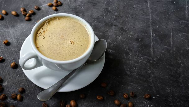 Horizontal banner with a cup of coffee and coffee beans on a dark concrete background. View from above. Copy space. Espresso or Americano in a cup. - Photo, Image