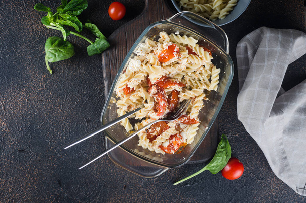 Italian dish of  pasta mixing with Feta cheese baked and tomatoes on a dark background. Fetapasta. Trending viral recipe, Flat lay, copy space - Φωτογραφία, εικόνα