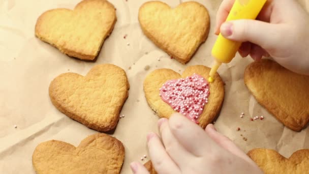 donna decora biscotti a forma di cuore con glassa gialla, primo piano, processo di cottura, concetto romantico - Filmati, video