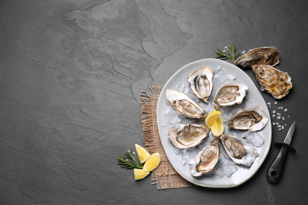 Delicious fresh oysters with lemon slices served on black slate table, flat lay. Space for text - Foto, Imagen