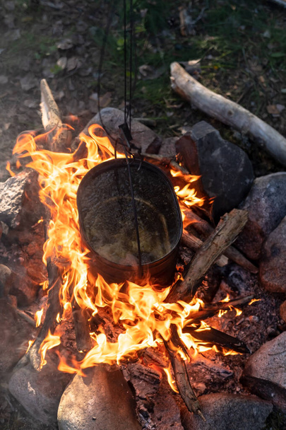 Pot of boiling water hangs over a campfire flame. Cooking in the camp. Active lifestyle. - Zdjęcie, obraz