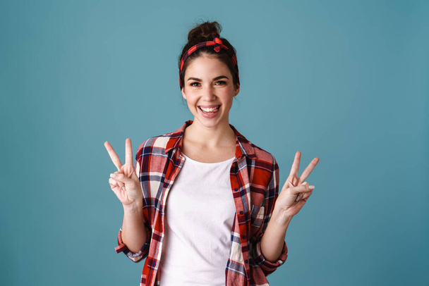 Happy beautiful brunette girl smiling and gesturing peace sign isolated over blue background - Foto, immagini