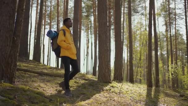 African czarny człowiek wspina się pod górę w lesie w żółtej kurtce z plecakiem w zwolnionym tempie - Materiał filmowy, wideo