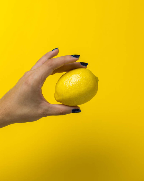 one hand holding one lemon in a yellow background - Foto, Imagem