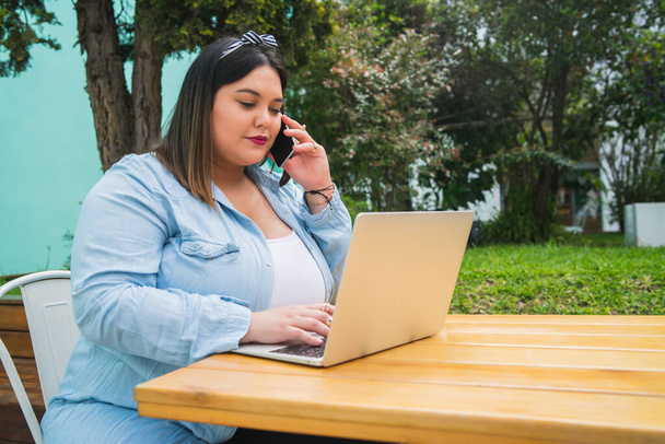 Plus size woman talking on the phone and using laptop. - Foto, imagen