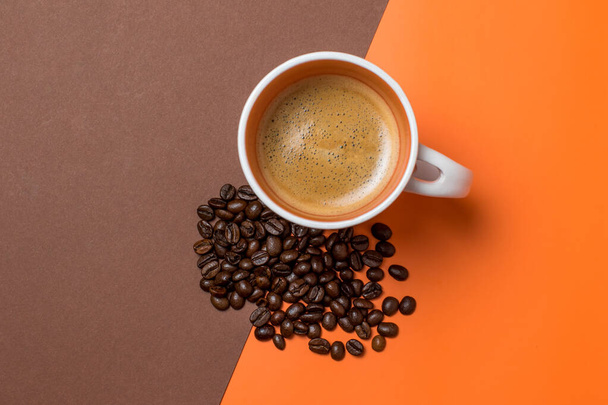 coffee in a white coffee cup and many coffee beans placed in a brown and orange background - Foto, Imagen
