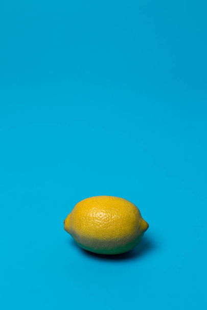 one yellow lemon in a blue background. Analog colors - Zdjęcie, obraz