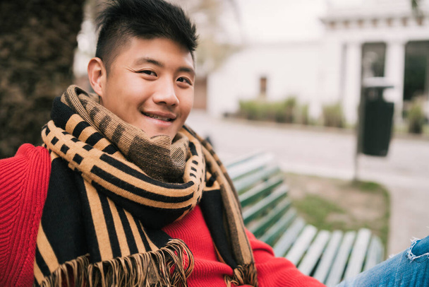 Asian man sitting on a bench in park. - 写真・画像