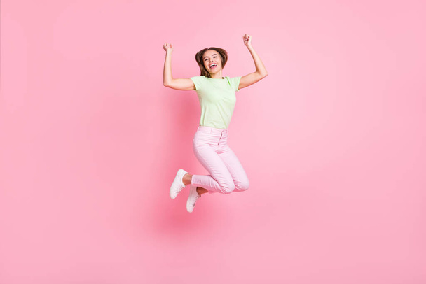 Full size photo of cheerful carefree young girl jumping fists up celebrate isolated on pink color background - Φωτογραφία, εικόνα