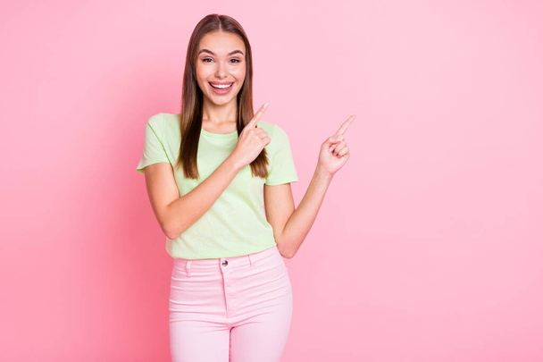 Photo of sweet adorable young lady wear green t-shirt smiling pointing empty space isolated pastel pink color background - Φωτογραφία, εικόνα