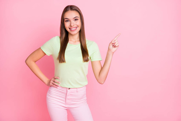 Photo of cute pretty young girl dressed green t-shirt pointing empty space isolated pastel pink color background - Zdjęcie, obraz