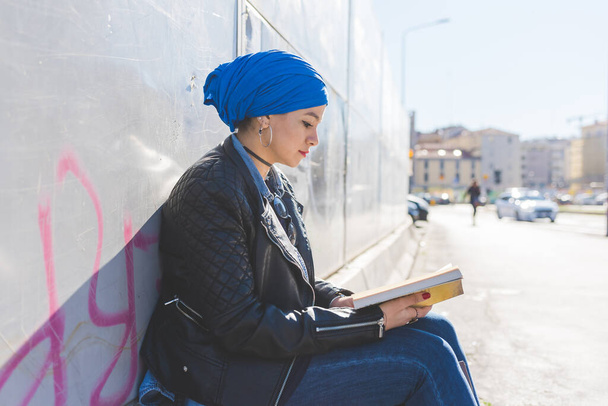 アラビア語の若い女性を身に着けているヒジャーブ屋外読書本 - 写真・画像