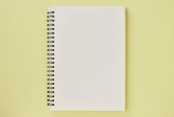 Cuaderno espiral o cuaderno de primavera en tipo sin forro sobre fondo minimalista amarillo pastel. Cuaderno espiral Mock up en el marco del centro - Foto, imagen