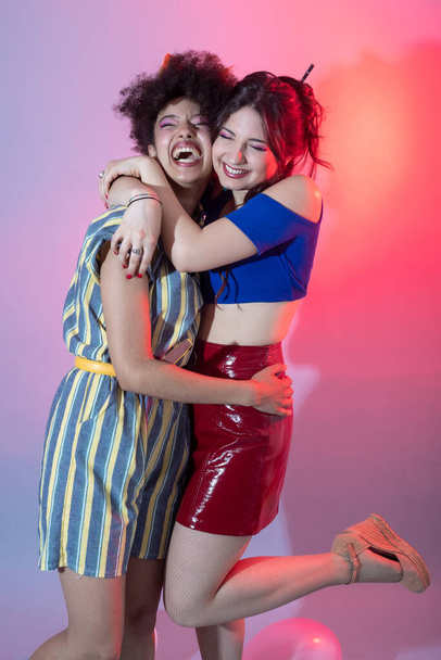Дві молоді багатонаціональні жінки сміються обіймаючи ізольований фон
 - Фото, зображення