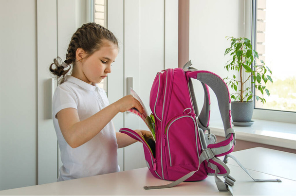 Школярка в шкільному одязі готується до школи і збирає блокнот у портфелі
. - Фото, зображення