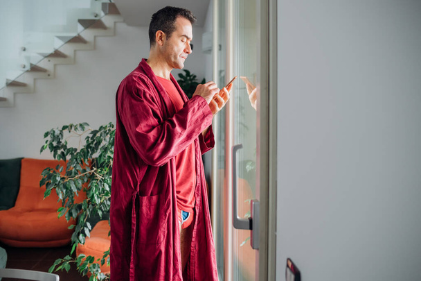 Homem adulto interior em casa homewear usando smartphone verificando feed de notícias  - Foto, Imagem