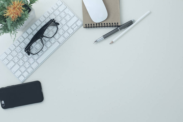 Witte compacte toetsenbord muis bril pen potlood notitieblok telefoon bloem in een pot op witte achtergrond - Foto, afbeelding