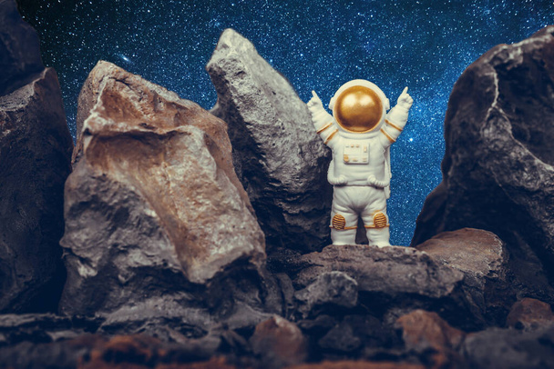 Zadowolony astronauta podnoszący ramiona stojąc na skalistej górze. Kosmonauta w białym skafandrze i kasku. Koncepcja kosmonautyki, podróży kosmicznych, wolności i zwycięstwa. - Zdjęcie, obraz