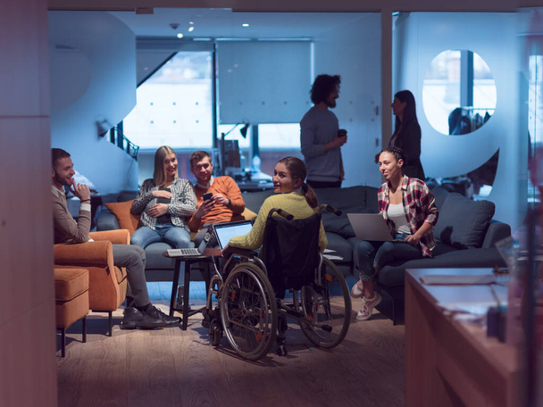 Handicapped businesswoman in a wheelchair on meeting with her diverse business team brainstorming about ideas and plans in a modern open space coworking office space. High quality photo - Фото, зображення