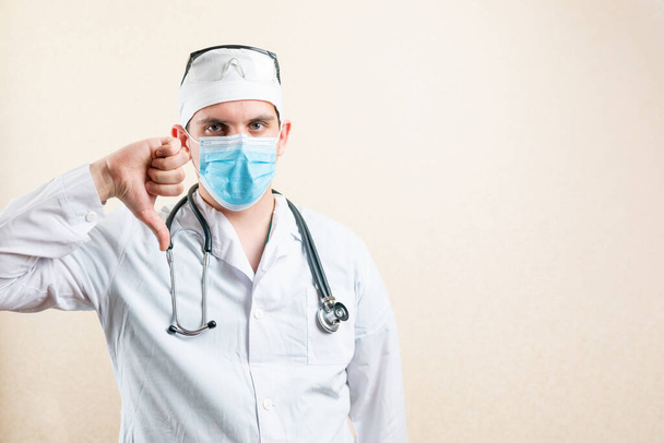 Doutor em máscara e boné, mostrando os polegares para baixo. Foto de alta qualidade - Foto, Imagem