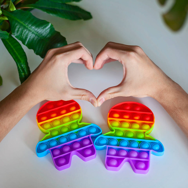 Руки людини у формі серця біля двох фігур з барвистим веселковим прапором, концепція гомосексуальної гордості
 - Фото, зображення