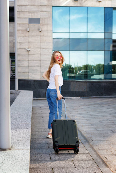 Egy szőke nő boldog a bőrönddel, nyaranta utazik. Repülővel történő utazás - Fotó, kép