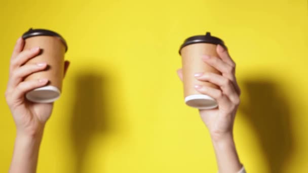 Dwie kawy specjalna oferta lub promocja. Ręce trzymające dwie filiżanki na żółtym tle ekranu. Herbata lub kawa na wynos. Brązowy kubek papierowy z czarną pokrywą. - Materiał filmowy, wideo