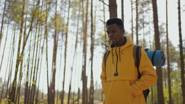 African black man climbs uphill in woods in yellow jacket with backpack in slow motion - Footage, Video
