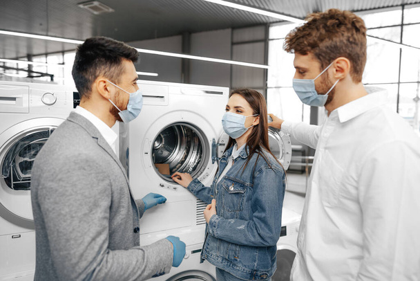 Salesman in hypermarket wearing medical mask demonstrates his clients a new washing machine - Фото, зображення