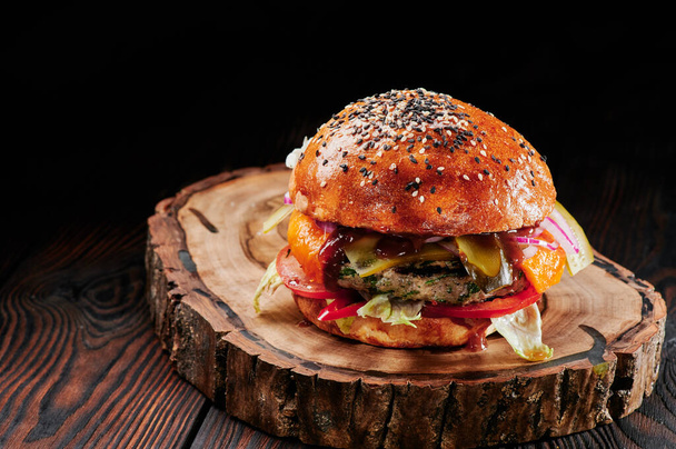 Beef burger with cheese, tomatoes, red onions, cucumber and lettuce on wooden cut on black background. Space for text. Unhealthy food. - Photo, Image