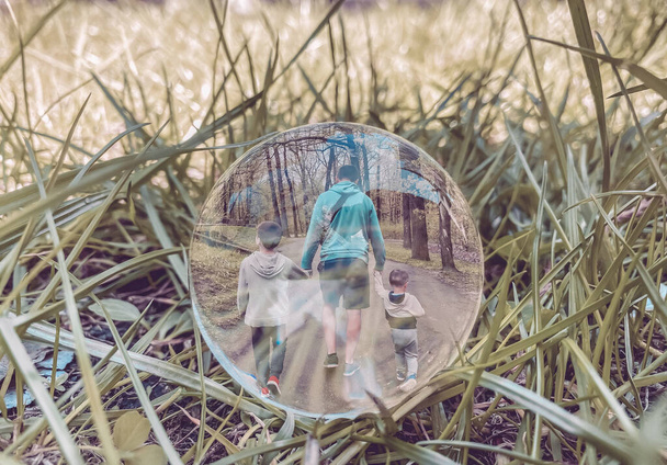 En la hierba en el claro se encuentra una bola de vidrio en la que la vista desde la parte posterior de un hombre que camina y dos niños, un padre y los hijos. - Foto, Imagen